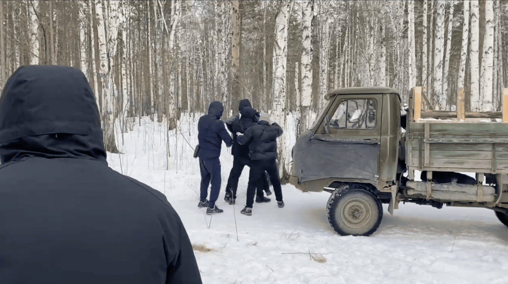 Охранники оттесняют мужчину, который хотел преградить путь в рощу машине с опорами для забора